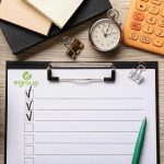Checklist de egroup sobre indicadores de capacitación, con cronómetro, calculadora y taza de café sobre un escritorio de oficina